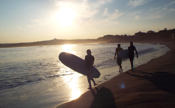 Three Ecoswell interns carrying surfboards across a beach as the sun rises